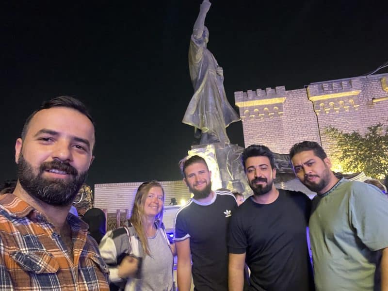 Ali Babylon tour guide and four guests taking a group selfie in front of the Al-Mutanabbi statue at night in Baghdad, Iraq