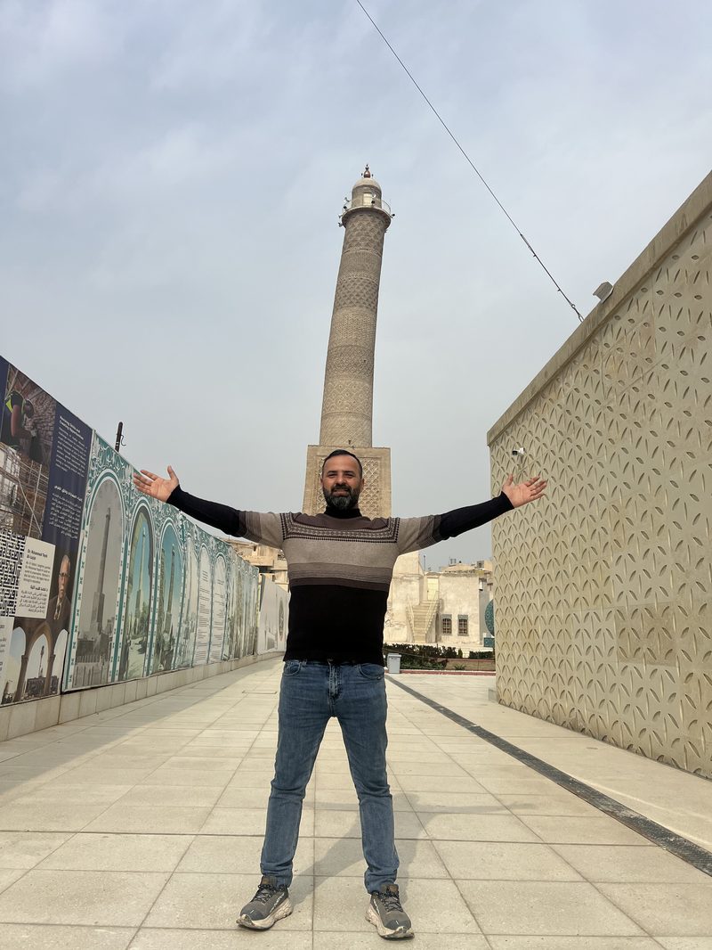 Tour guide posing with arms outstretched in front of the reconstructed Al-Hadba leaning minaret in Mosul, Iraq