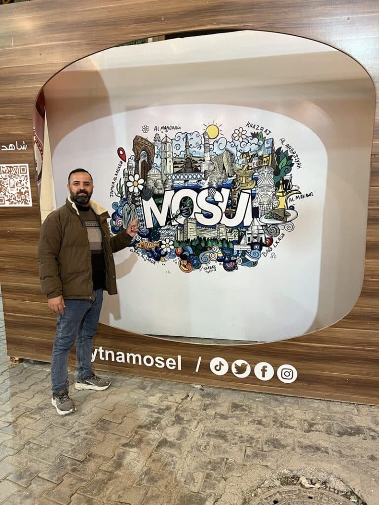 Tour guide standing next to a colorful Mosul city illustration mural at a tourist attraction in Mosul, Iraq