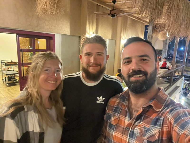 Ali Babylon tour guide posing with a European couple at a traditional Iraqi restaurant with thatched ceiling decor
