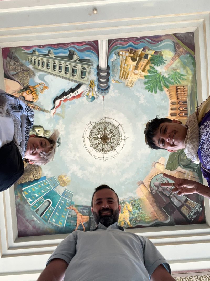 Ali Babylon tour guide and two female tourists posing under the decorative ceiling painting inside Saddam Hussein's Palace near Babylon, Iraq