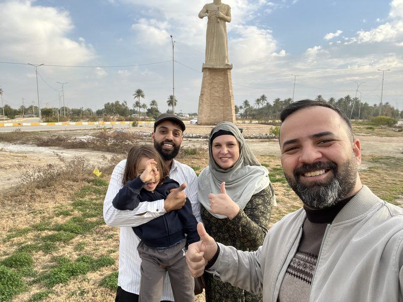 Ali Babylon tour guide taking a group selfie with an Iraqi family including a child in front of a large monument statue in Baghdad
