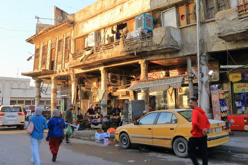 Street life scene with old buildings and yellow car in Baghdad, Iraq