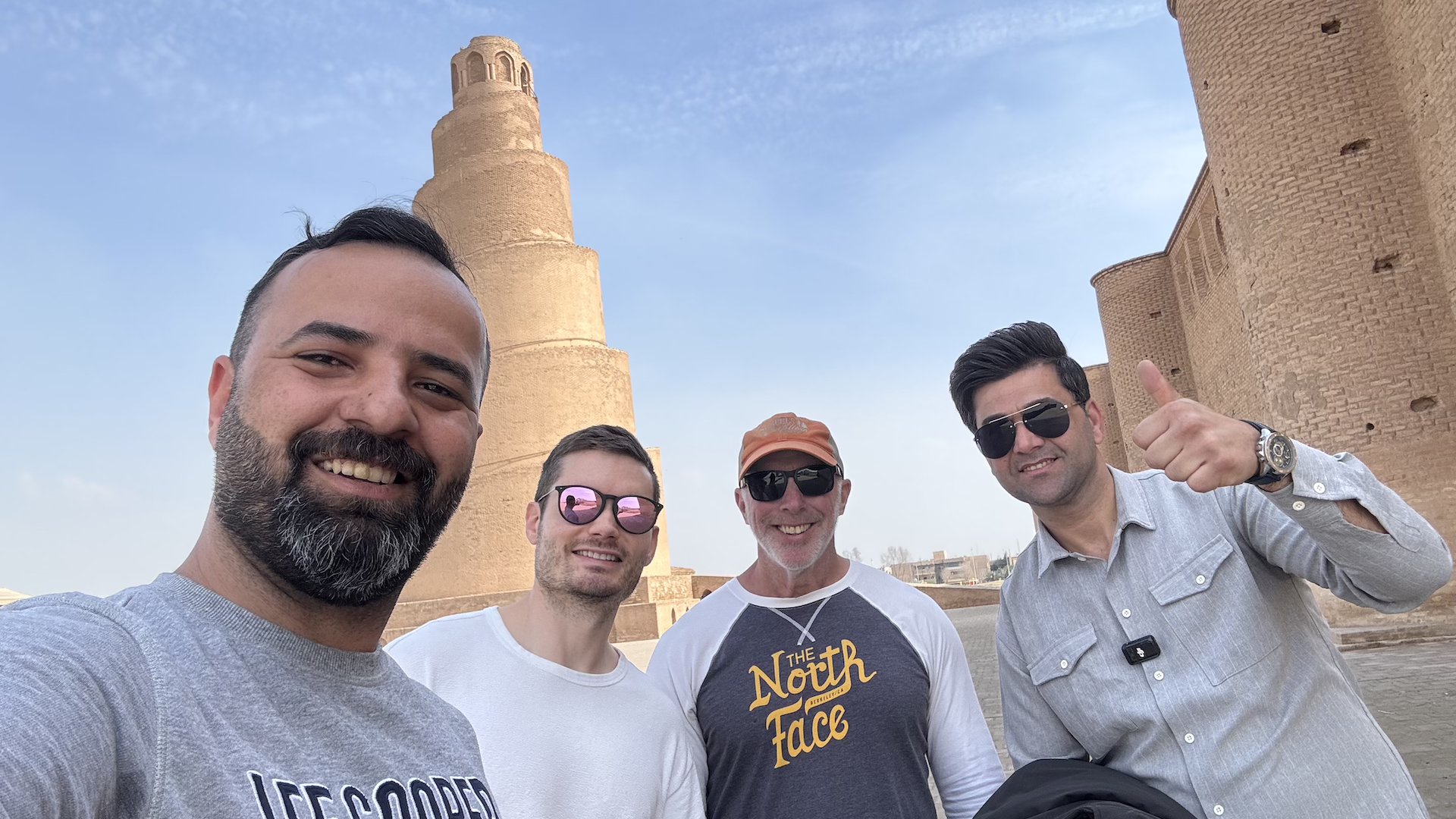 Travelers smiling at the base of the Malwiya spiral minaret in Samarra, Iraq — one of the ancient world's most iconic landmarks.
