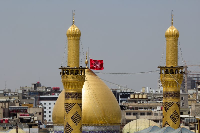 Golden domes and minarets of the Imam Hussein shrine with red flag in Karbala, Iraq