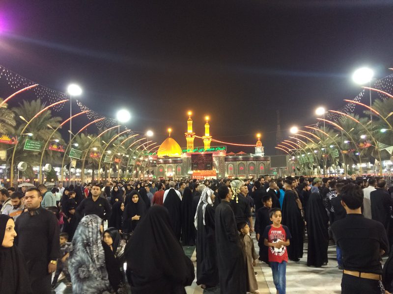 Crowds of pilgrims walking toward the illuminated Imam Hussein shrine at night in Karbala, Iraq