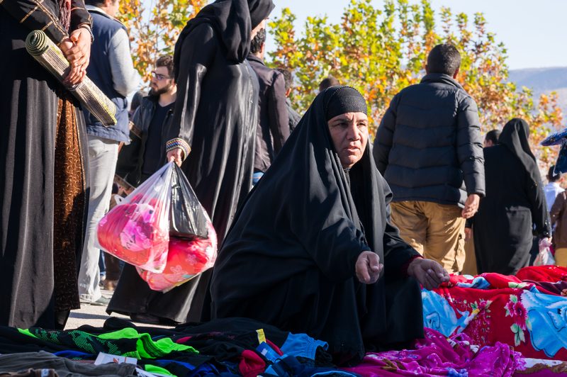 Iraqi woman in black abaya selling colorful clothes at an outdoor market in Kurdistan, Iraq