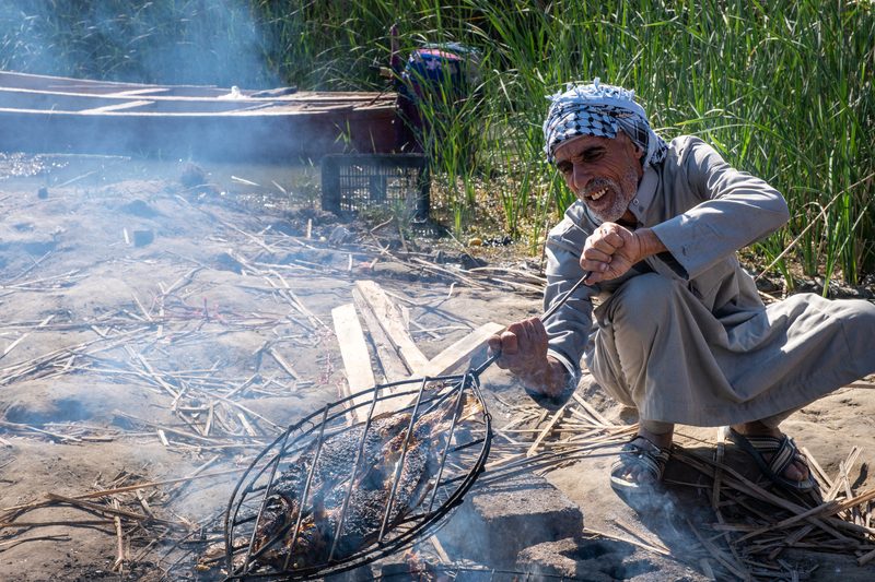 Marsh Arab man grilling fish over an open fire on the banks of the Iraqi marshes
